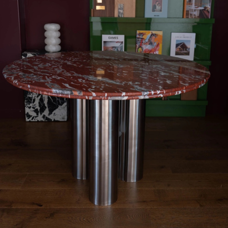 Close-up of red marble round table with stainless steel cylindrical bases - smooth polished stone surface